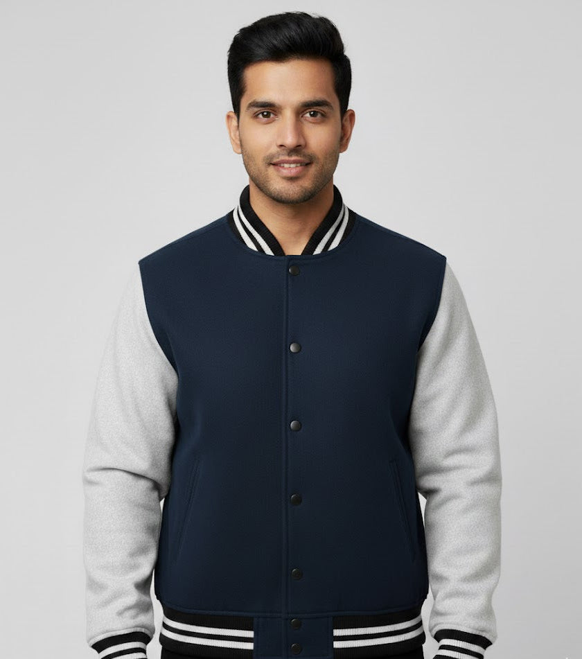 Man wearing a navy and gray varsity jacket on a light gray background